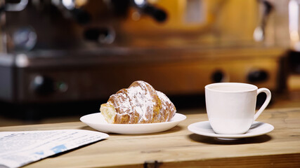 cup of coffee near tasty croissant and newspaper on table.