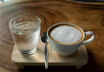 Hot coffee and a glass of water on a wooden coffee shop table.