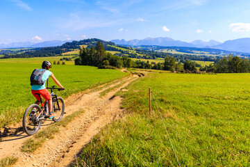 Young woman riding bike on rural road with beautiful panorama of Tatra Mountains in distance, Poland