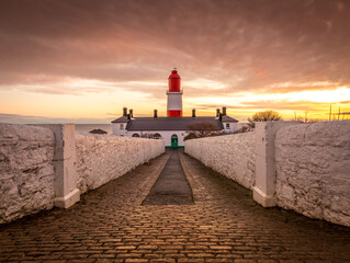 The pathway to the red and white striped, 23 meter tall,  Souter Lighthouse in Marsden, South Shields as the sun rises - obrazy, fototapety, plakaty