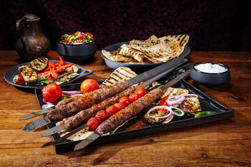 Traditional Turk Adana kebap on shashlik skewer with barbecue vegetable, flatbread and yogurt as close-up on a rustic metal tray