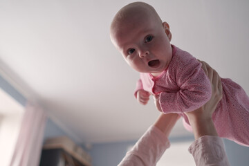 Portrait of caucasian mother lifting and playing with newborn baby, baby talking to mother.