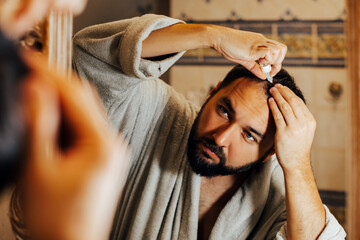 Hair Loss concept. Man takes care of his hair at home in the bathroom, rubs in ampoules against...