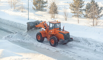 Big orange tractor cleans up snow from the road and loads it into the truck. Cleaning and cleaning...