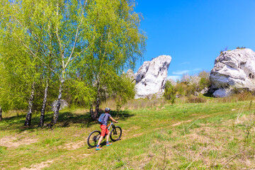 Mountain biker climbing on trail leading to lime rocks formation near Rzedkowice village in Polish Jurassic Highland on sunny spring day, Poland
