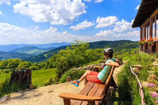 Woman in cycling outfit sitting on bench in front of Wierchomla refuge in Beskid Sadecki mountain on nice sunny day, Poland