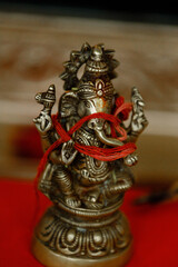 Fototapeta premium The Hindu god Ganesha statue Idol of Hindu god Ganesh covered with red thread stands on the table at the Indian wedding Indian Wedding Ceremony Cropped photo Close up