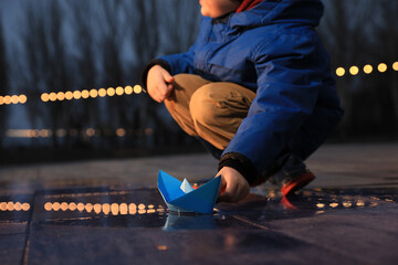 Fototapeta na wymiar Little boy playing with paper boat near puddle outdoors, closeup