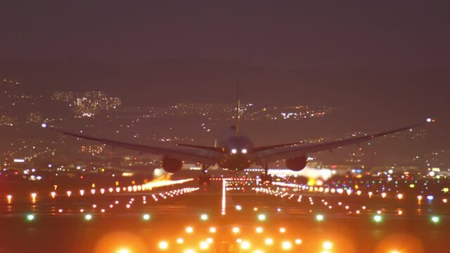 Passenger aircraft landing at night, telephoto view from end of runway with straight perspective. Bright approach and edge lights, flashlights at tail and wings of airliner
