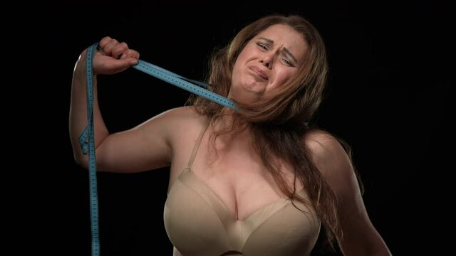 Medium shot overweight woman chocking with measuring tape at black background. Concept of social beauty standard and incompliance. Body positive