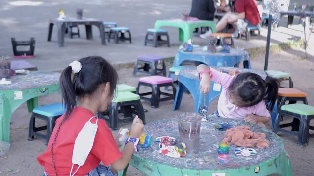 Slow motion scene of 5-year-old Asian girl sits and paints plaster cartoon characters.