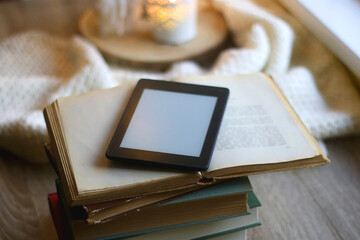 Stack of books, digital e-reader and lit candles. Selective focus.