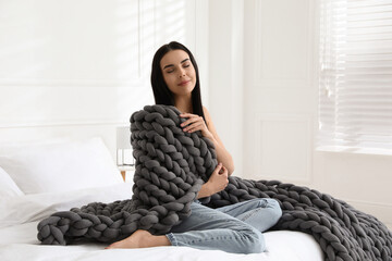 Young woman with chunky knit blanket on bed at home