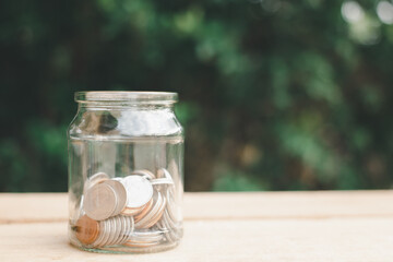 Coins in half clear jar placed on wooden planks outdoors in the garden, investment saving concept.copy space.