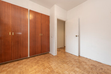Double built-in wardrobe with mahogany doors and light oak parquet floors in empty room