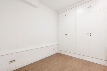 Empty white painted room with reddish marble floors and fitted wardrobes with white doors