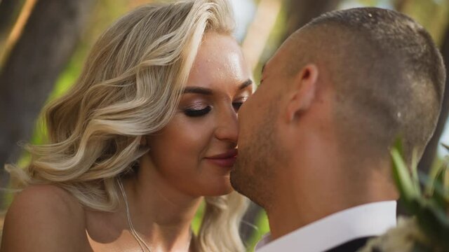 Gentle guy groom in festive suit kisses beloved happy blonde woman bride standing together in sunny spring forest close view slow motion