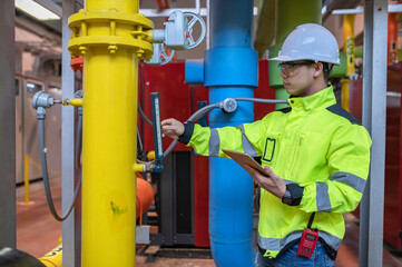 Asian engineer wearing glasses working in the boiler room,maintenance checking technical data of heating system equipment,Thailand people