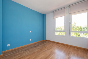 Empty room with blue wall, oak flooring and large windows