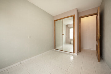 Empty room with brown and gray walls and white porcelain floors and fitted wardrobe with mirrored doors