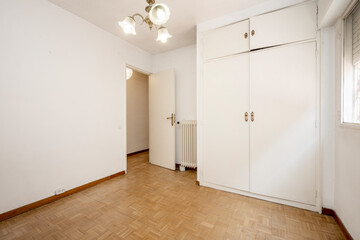 Empty room with white walls and oak parquet floors and fitted wardrobe with white doors
