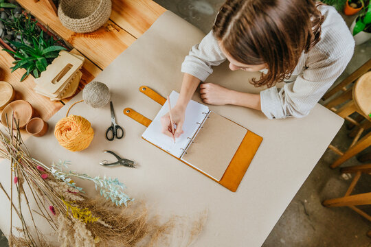 Young woman writing a business plan sitting at the table working at her workshop