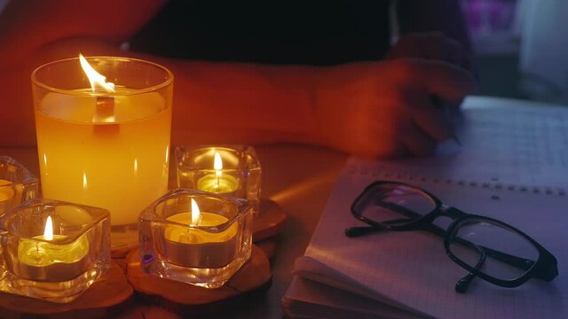 A woman writeWoman writes story or novella in large notebook by candlelight. Candles are lit on table in candlesticks and woman makes notes in notebook. Atmospheric cinematic scene. Video. Static