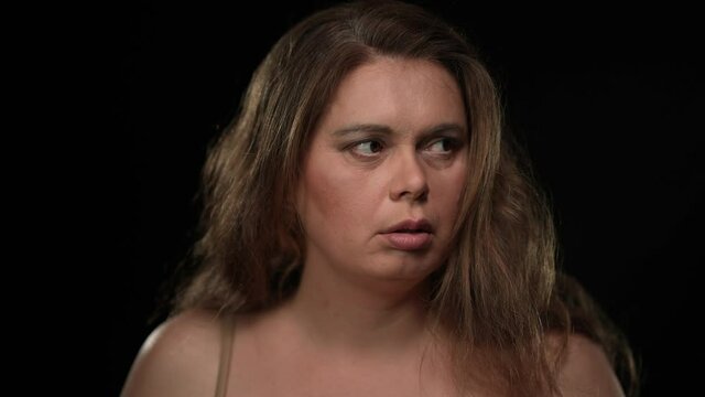 Close-up portrait scared plus size woman looking around with worried facial expression closing face with hands. Stressed frightened Caucasian lady hiding from danger posing at black background