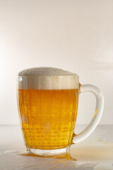 A beer mug full of intoxicating drink and foam. A glass of beer, with a handle, with light beer and thick foam.