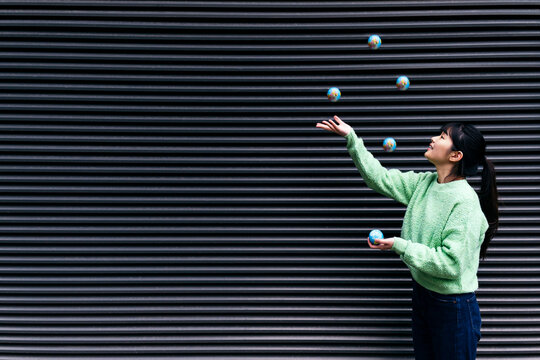 Young woman juggling globes by black corrugated wall