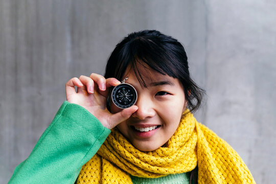 Happy woman with navigational compass in front of eye