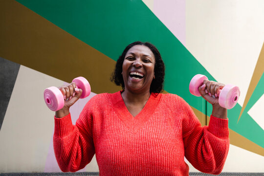 Cheerful woman exercising with pink dumbbells