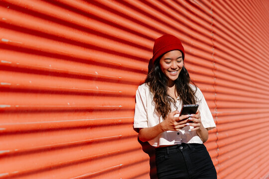 Smiling woman using mobile phone at red corrugated wall