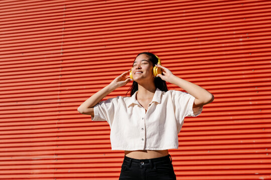 Smiling woman listening music through headphones in front of corrugated wall