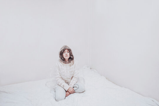 Bored woman with eyes closed sitting on duvet in confined place
