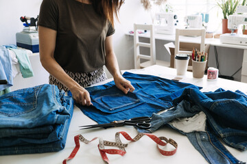 Sustainable fashion, Denim Upcycling Ideas, Using Old Jeans, Repurposing Jeans, Reusing Old Jeans, Upcycle Stuff. Woman seamstress cut and repair old blue jeans in sewing studio.