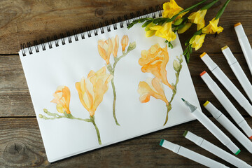 Flat lay composition with beautiful drawing of freesia flowers in sketchbook on wooden table