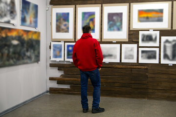 A man looks at paintings at an exhibition in an art gallery. Leisure in the city.