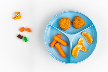 Kids meal containing chicken nuggets, carrots and tangerine pieces on white background with toy block pieces spread on it