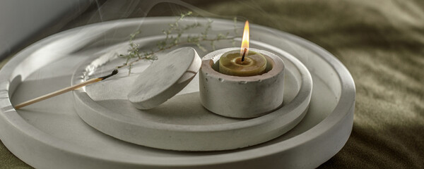 Olive green burning tea light candle and a match with which it was lit in white minimalistic concrete candlestick. Modern concrete home accessories. Relaxation and meditation concept