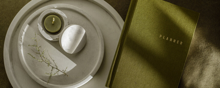 Olive green planner and tea light candle in white minimalistic concrete candlestick. Notebook and stationery. Concrete modern home accessories.