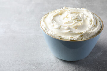 Bowl of tasty cream cheese on light grey table, space for text