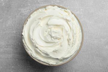 Bowl of tasty cream cheese on light grey table, top view