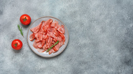 Slices of prosciutto di parma or jamon serrano in a plate on gray grunge background. Top view, flat...