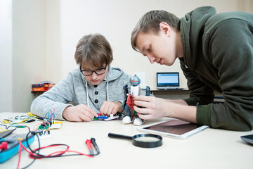 Teenager boy with instructor at robotics school makes robot managed from the constructor, child learns robot constructing.
