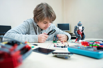 Teenager boy at robotics school makes robot managed from the constructor, child learns robot...