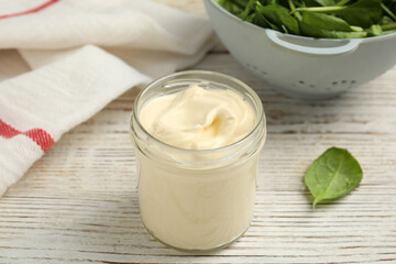 Jar of delicious mayonnaise and fresh spinach on white wooden table