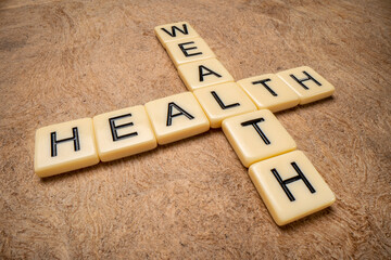 health and wealth crossword in ivory letter tiles against textured handmade paper, wellbeing concept