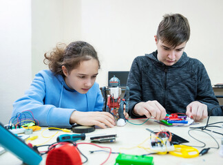 Obraz premium Teenager boy and girl at robotics school makes robot managed from the constructor, child learns robot constructing.