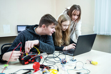 Diverse teenager pupils build robot vehicle learning at table at STEM engineering science education class. School students making robotic cars using laptop computer. - obrazy, fototapety, plakaty